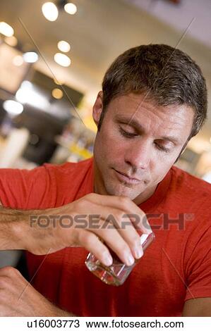 Stock Image - Man holding and looking into cocktail glass. Fotosearch