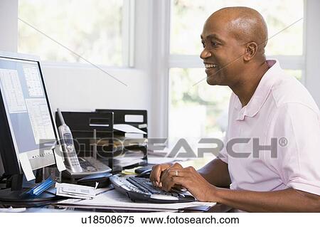 Stock Photography - Man in home office using computer and smiling. Fotosearch
