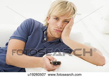 Stock Photo - Man in living room holding remote control. Fotosearch