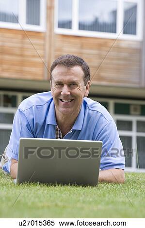 Stock Photography - Man lying on lawn of school with laptop. Fotosearch