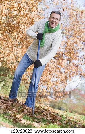 Man outdoors raking leaves and smiling (selective focus) View Large Photo Image Stock Photo - Man outdoors raking leaves and smiling (selective focus). Fotosearch