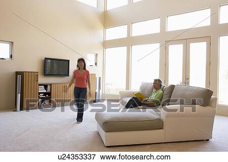 Man reading book in living room with woman walking by View Large Photo Image Stock Photo - Man reading book in living room with woman walking by. Fotosearch