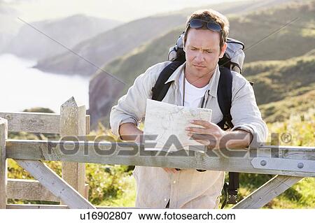 Stock Photo - Man relaxing on cliffside path holding map. Fotosearch