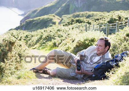 Stock Photograph - Man relaxing on cliffside path. Fotosearch