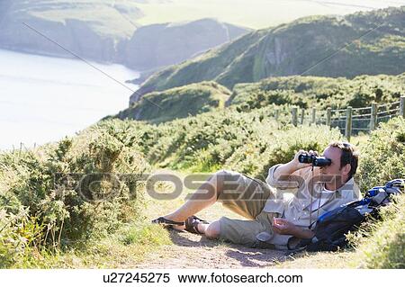 Man relaxing on cliffside path using binoculars View Large Photo Image Stock Photography - Man relaxing on cliffside path using binoculars. Fotosearch
