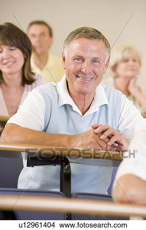 Picture - Man sitting in adult classroom with students in background (selective focus). Fotosearch