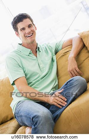 Stock Photo - Man sitting in living room laughing. Fotosearch