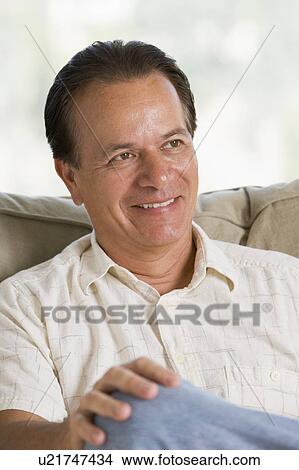 Picture - Man sitting in living room smiling. Fotosearch
