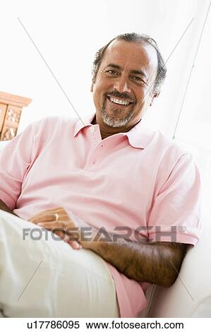 Stock Photography - Man sitting in living room smiling (high key). Fotosearch