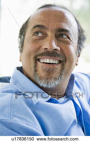 Stock Image - Man sitting indoors looking up and smiling (high key). Fotosearch