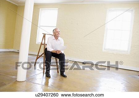 Man sitting on ladder in empty space holding paper smiling View Large Photo Image Stock Image - Man sitting on ladder in empty space holding paper smiling. Fotosearch