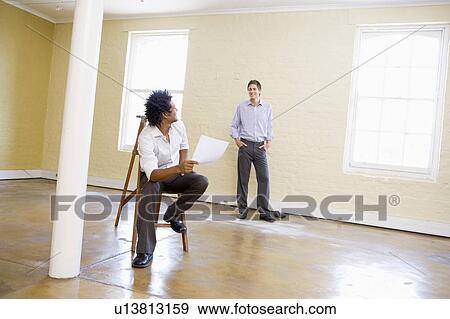 Man sitting on ladder in empty space holding paper talking to other man View Large Photo Image Stock Photo - Man sitting on ladder in empty space holding paper talking to other man. Fotosearch