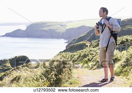 Man standing on cliffside path View Large Photo Image Stock Image - Man standing on cliffside path. Fotosearch