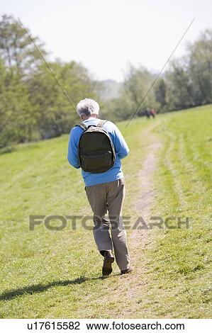 Stock Image - Man walking outdoors with people in background. Fotosearch