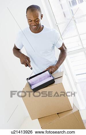 Stock Photograph - Man with roller and paint in new home smiling. Fotosearch
