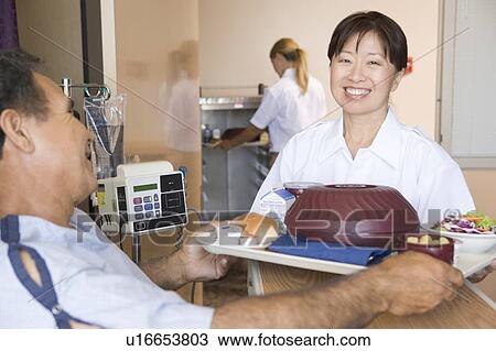 Stock Image - Nurse Serving A Patient A Meal In His Bed. Fotosearch