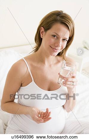 Pregnant woman in bedroom holding medicine and water smiling View Large Photo Image Stock Photograph - Pregnant woman in bedroom holding medicine and water smiling. Fotosearch