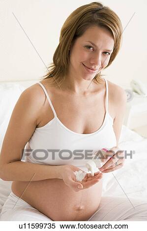 Stock Photography - Pregnant woman in bedroom with medicine smiling. Fotosearch