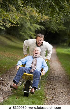 Son pushing senior father in wheelbarrow View Large Photo Image Stock Photo - Son pushing senior father in wheelbarrow. Fotosearch