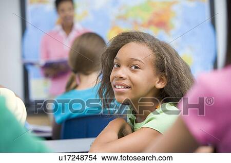 Student in class looking at camera with teacher in background (selective focus) View Large Photo Image Picture - Student in class looking at camera with teacher in background (selective focus). Fotosearch