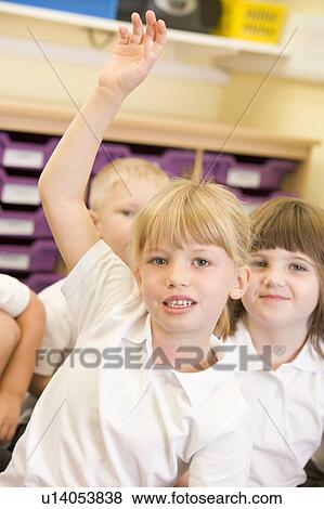 Stock Photo - Student in class volunteering with students in background (selective focus). Fotosearch
