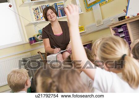 Picture - Teacher in class with student volunteering in foreground (selective focus). Fotosearch