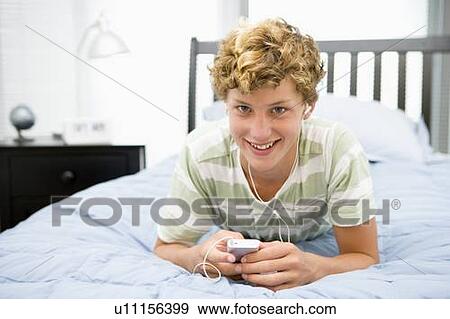 Stock Photo - Teenage Boy Lying On Bed Listening To Mp3 Player. Fotosearch