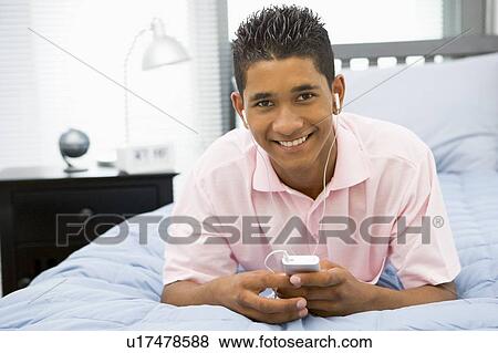 Stock Photo - Teenage Boy Lying On Bed Listening To Mp3 Player. Fotosearch