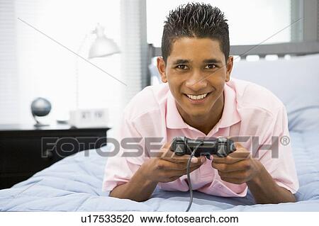 Stock Image - Teenage Boy Lying On Bed Playing Video Game. Fotosearch