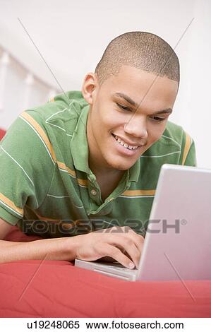 Stock Photography - Teenage Boy Lying On Bed Using Laptop . Fotosearch