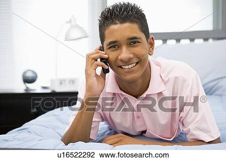 Stock Image - Teenage Boy Lying On Bed Using Mobile Phone . Fotosearch