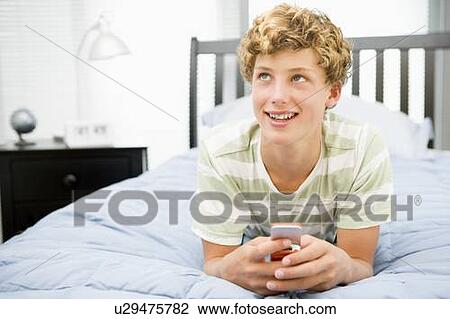 Stock Image - Teenage Boy Lying On Bed Using Mobile Phone . Fotosearch