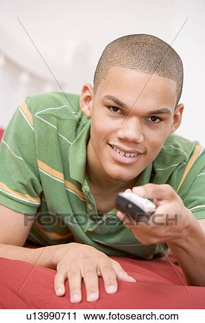 Stock Image - Teenage Boy Lying On Bed Using Remote. Fotosearch