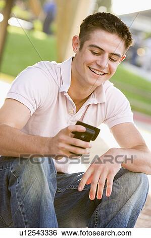 Teenage Boy Sitting Outdoors Using Mobile Phone View Large Photo Image Stock Photograph - Teenage Boy Sitting Outdoors Using Mobile Phone. Fotosearch