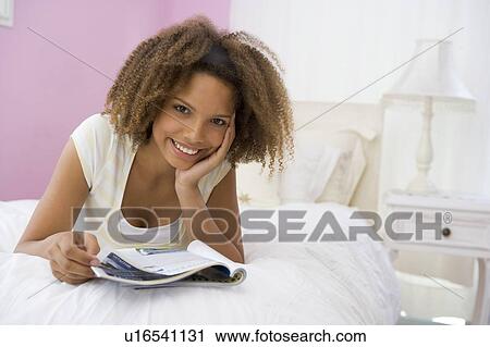 Stock Image - Teenage Girl Lying On Bed Reading. Fotosearch