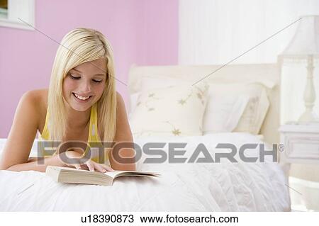 Stock Image - Teenage Girl Lying On Bed Reading. Fotosearch