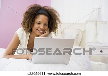 Stock Image - Teenage Girl Lying On Bed Using Laptop . Fotosearch