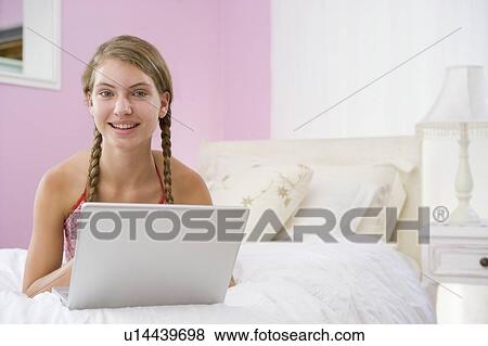 Stock Photo - Teenage Girl Lying On Bed Using Laptop . Fotosearch