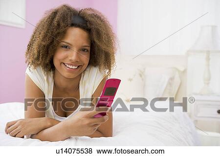 Stock Photo - Teenage Girl Lying On Bed Using Mobile Phone . Fotosearch
