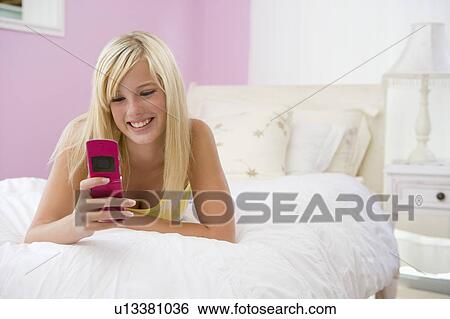 Stock Photograph - Teenage Girl Lying On Bed Using Mobile Phone . Fotosearch