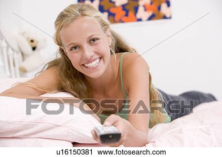Stock Image - Teenage Girl Lying On Her Bed Changing Television Channels. Fotosearch