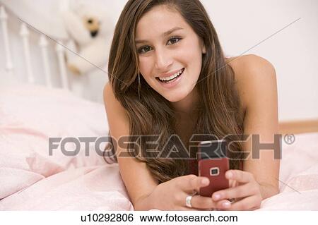 Stock Photograph - Teenage Girl Lying On Her Bed Using Mobile Phone. Fotosearch