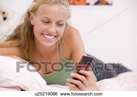 Stock Photograph - Teenage Girl Lying On Her Bed Using Mobile Phone. Fotosearch