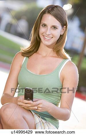 Stock Photo - Teenage Girl Sitting Outdoors Using Mobile Phone. Fotosearch