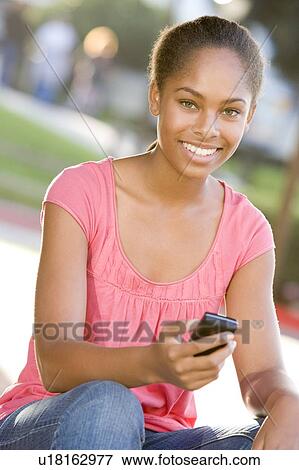 Teenage Girl Sitting Outdoors Using Mobile Phone View Large Photo Image Stock Photo - Teenage Girl Sitting Outdoors Using Mobile Phone. Fotosearch
