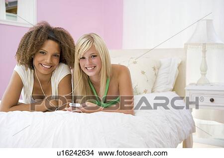 Picture - Teenage Girls Lying On Bed Listening To Mp3 Player. Fotosearch