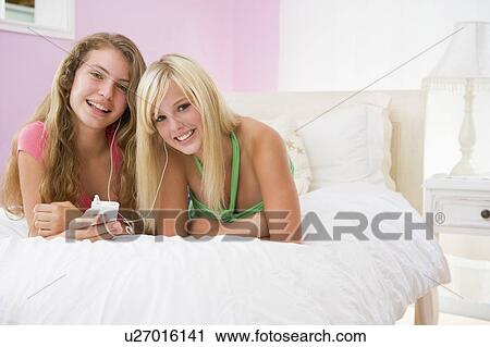 Stock Image - Teenage Girls Lying On Bed Listening To Mp3 Player. Fotosearch