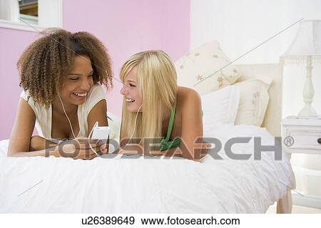 Stock Photo - Teenage Girls Lying On Bed Listening To Mp3 Player. Fotosearch
