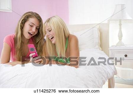 Stock Photograph - Teenage Girls Lying On Bed Using Cell Phone . Fotosearch