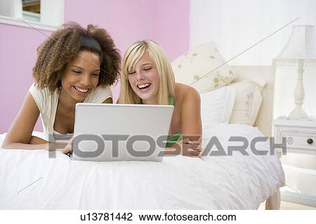 Stock Image - Teenage Girls Lying On Bed Using Laptop . Fotosearch